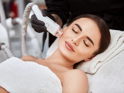 close-up of pretty girl receiving facial treatment with laser by beautician in spa salon, pleasent woman lying with her eyes closed and getting face theraphy
